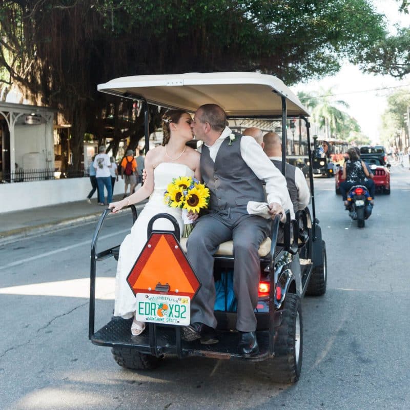 a couple kisses on the back of a golf cart after getting married